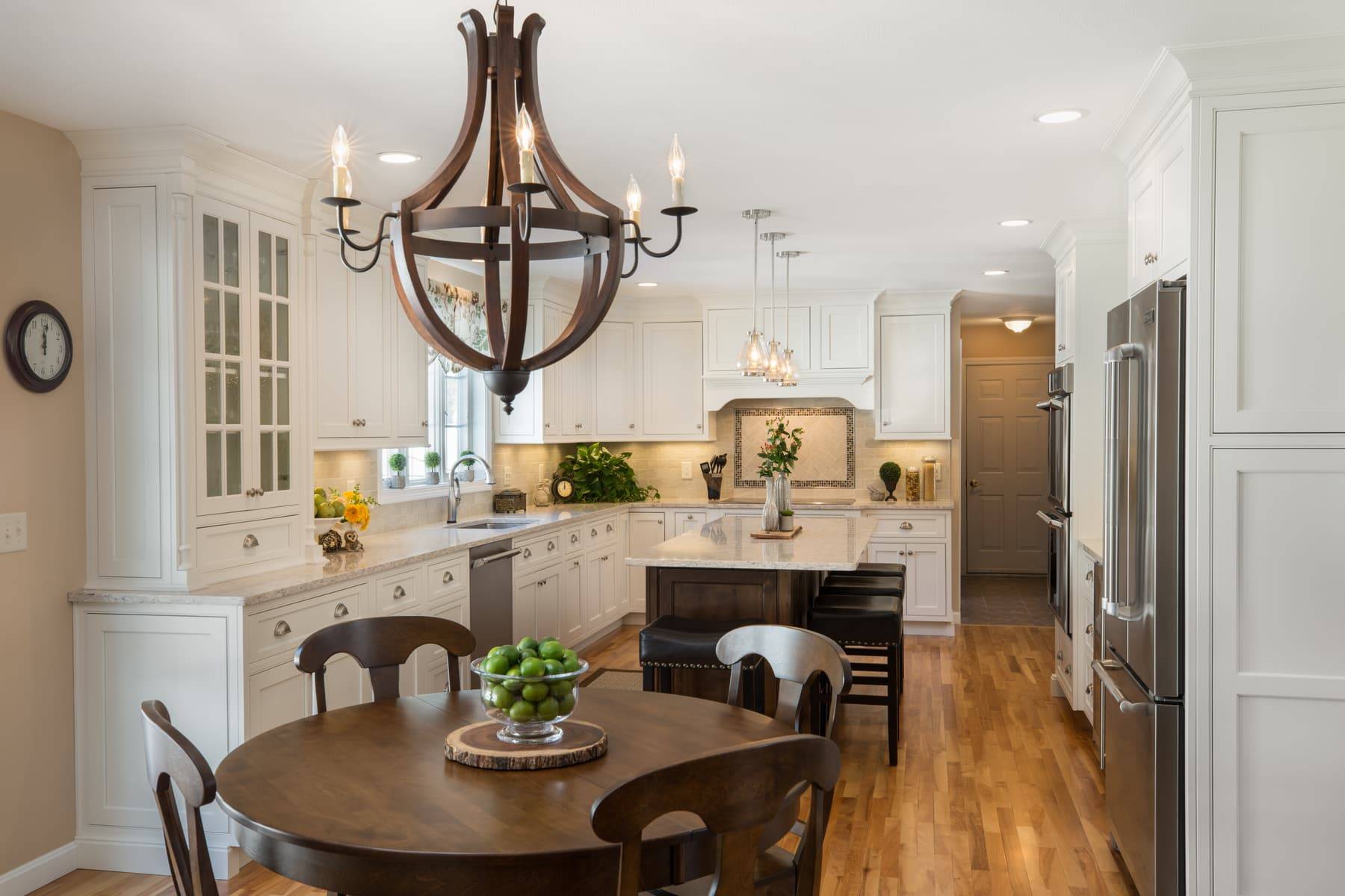 White kitchen cabinetry, a dark island, and a wood dining chandelier in a Plaistow, New Hampshire home